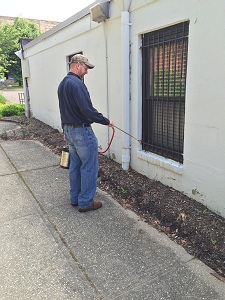 exterminator is spraying insecticides outside house